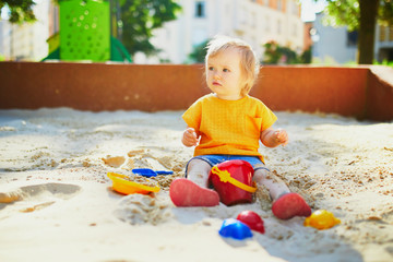 Adorable little girl having fun on playground in sandpit