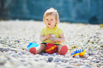 Adorable toddler girl playing with pebbles on the beach