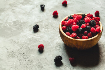 raspberries and blackberries in wood bowl on gray table, vintage