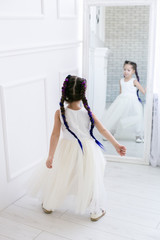 vertical portrait of a five year old girl standing in front of a mirror in a white studio