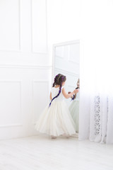vertical portrait of a five year old girl in a white dress standing in front of a mirror in a white studio