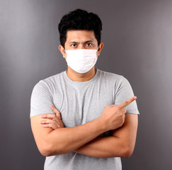 Portrait of handsome Asian man wearing a mask is sick Pointing finger isolated on Gray background in studio.