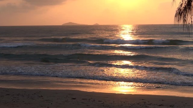 Dramatic sunrise at tropical sea. Calm seascape and golden sunrise reflection on the water with pine leaves in foreground and the island in background,4K time lapse video zoom out. 