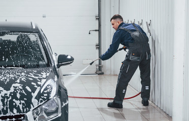 Fototapeta premium Male worker in uniform washing new modern car that covered with soap. Conception of service