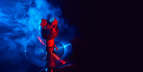 red hot shisha coals in a metal hookah bowl against a background of smoke