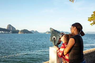 Mother helping a child in a lookout looking at sugar loaf in Copacabana, Rio de Janeiro, with the...