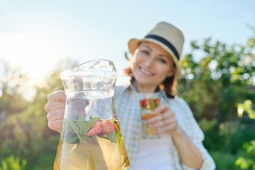 Fototapeta premium Close-up of jug and glass with mint strawberry drink in hands of woman