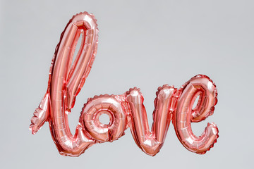 Love word from pink inflatable balloon floating in the air on grey background. The concept of...