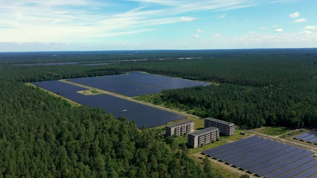 Drone footage panoramic shot of solar power station in Templin, Germany. Car is being driven in the background beetween solar panels and post-soviet buildings.
