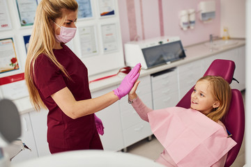 Gives high five. Little girl visiting dentist in clinic. Conception of stomatology