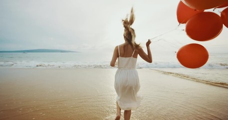 Beautiful woman in a white dress running on the beach holding red balloons, endless childhood freedom concept