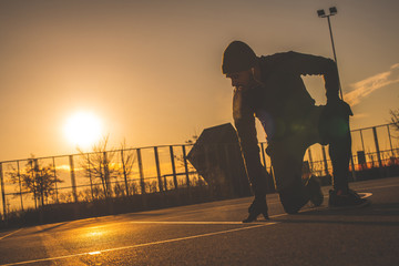 Young African American man doing stretch exercises, kneeling on one leg on the basketball court, at dawn