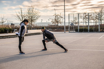 Young man and woman doing stretching exercises and talking on the sports field