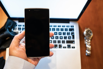 Businessman looking at his smart phone at the end of his working day.Laptop , watch and black tie on unfocused background End of the work day, time to relax concept