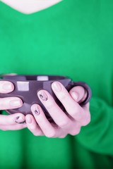 Beautiful female hands holding black cup on green background. Manicure with pink color nail polish,...