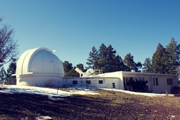 Fototapeta na wymiar Dome telescope at observatory, with pine trees and snow with clear blue sky