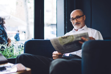 Senior man with newspaper sitting on chair near window