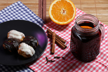 Glass of mulled wine, eclairs on a black plate, orange , cinnamon and cloves isolated on a black background.