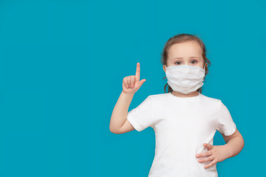 A little girl in a medical mask shows a symbolic hand gesture-warning, attention, on a blue background. Concept of medicine and healthcare in the fight against viruses. Cooy space. Mock up
