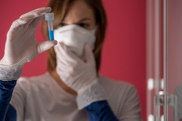 nurse wearing white surgical gloves and holding molded mask while examining a test tube with coronavirus flu vaccine in the medical laboratory to study a cure to stop the pandemic in the world