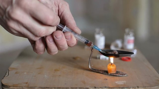 A drug addict draws a drug into a syringe and releases air from it. A male addict prepares to make an injection.