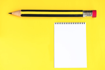 Paper notepad and huge pencil on the yellow background.