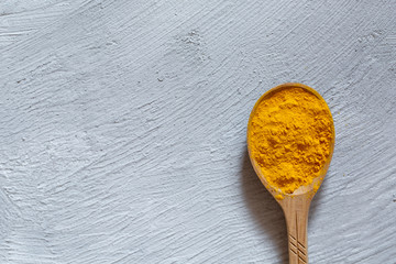 Natural medicine for immunity. Indian turmeric spice in a wooden spoon on a gray background.