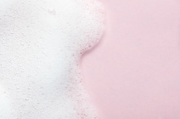 Foaming liquid on pink backdrop. Cosmetics foam background with copy space in right side. Cosmetic product sample of mousse, shampoo or soap. Skincare, cosmetology and beauty concept - obrazy, fototapety, plakaty
