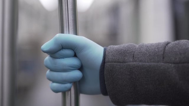 Man in the coat putting hand on the handrail in the subway wearing medical gloves during the pandemic coronavirus 