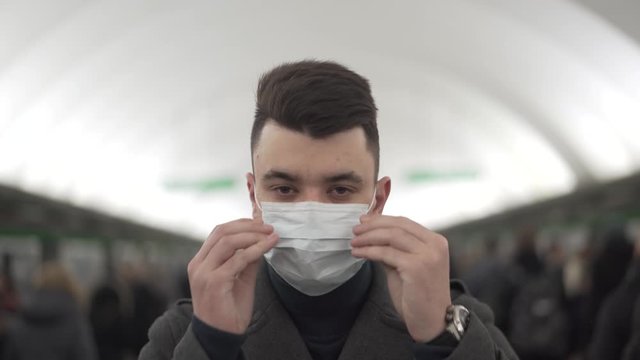Young business man in a coat standing in subway putting on the face mask during the quarantine pandemic period