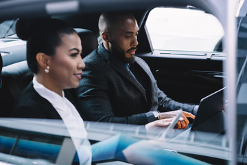 Pensive multiethnic coworkers using digital tablet in car