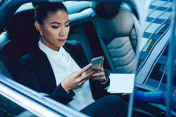 Calm ethnic businesswoman using smartphone in car