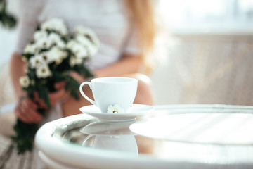 The girl drinks morning tea and enjoys life, admiring a bouquet of flowers .