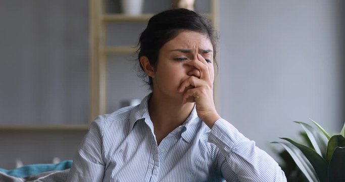 Stressed young indian woman sitting on couch, feeling frustrated. Unhappy millennial mixed race girl received bad news, experiencing grief alone. Worried lady regretting mistake or wrong choice.