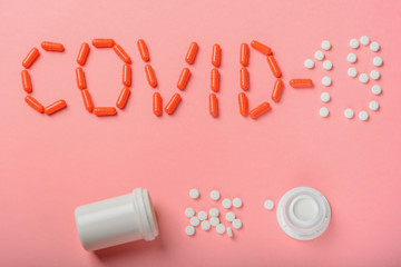 The inscription Covid-19 of tablets, medicines and plastic packaging on a pink background.