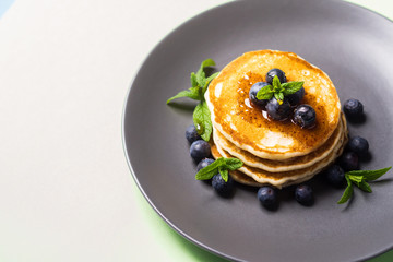 Stack of home made pancakes served with fresh berries and maple syrup on mint green pastel background. Simple and delicious breakfast