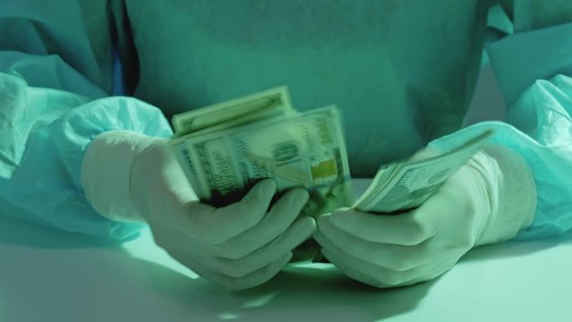 Expensive health maintenance. Fee-for-service medicine. Surgeon hands in gloves counting money.