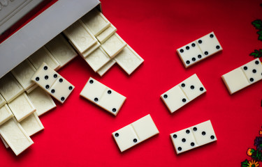 Domino Bones of dominoes fell out of a gray case on a red fabric background and a lot of space for text. View from above. 