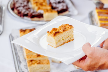 Sheet cake on plate is taken by a hand at wedding or birthday celebration