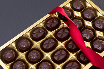 chocolate candies in a box with a red bow on a black background. dark photo, mood.