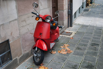 Red scooter parked by the wall in the empty street