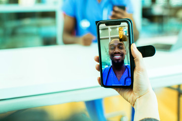 Portrait of a sick patient coughing into tissue being helped via tele medicine by a male doctor wearing blue scrubs uniform using smartphone mobile phone