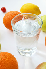 oranges, apples, lemon and a glass of water on a white background