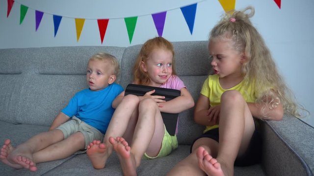 Kids arguing for playing with digital tablet on a sofa. Addictive friends