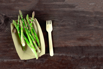 Fresh asparagus on eco plate with a fork on wooden table, closeup