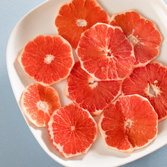 Sliced grapefruit rings in white plate on blue background . Copy space