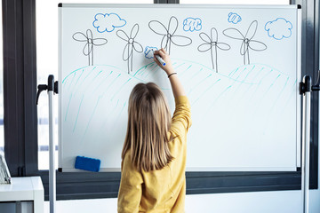 Little girl drawing a eolic park on a whiteboard with a marker pen at home.