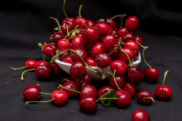 Obraz na płótnie Canvas Red cherries on black background coming out and hanging from the plate