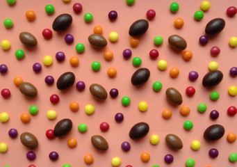 Several chocolate eggs and colorful candies on a peach background in a separate pattern