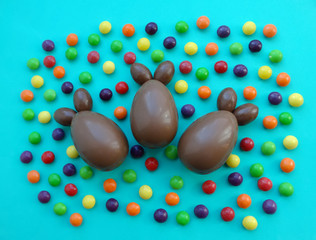 Top view of chocolate eggs in the form of rabbits and colored candies on a green background